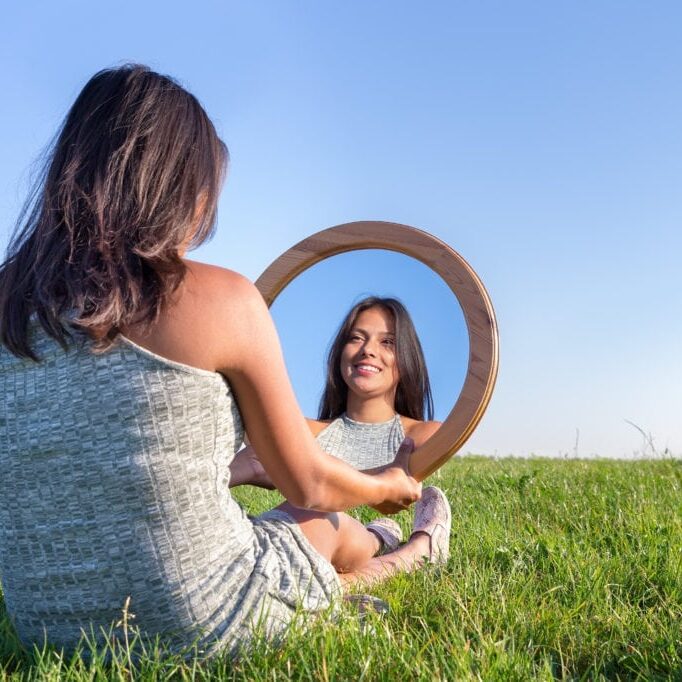 Woman sitting on grass looking at  her mirror image